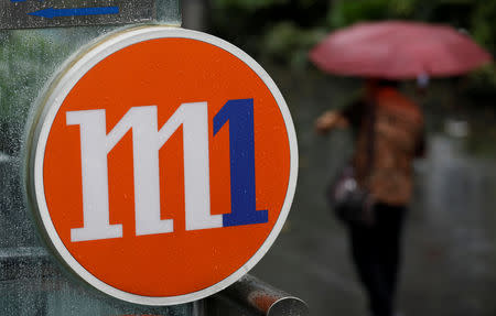 FILE PHOTO: A woman with an umbrella passes an M1 sign in Singapore April 7, 2017. REUTERS/Edgar Su/File Photo