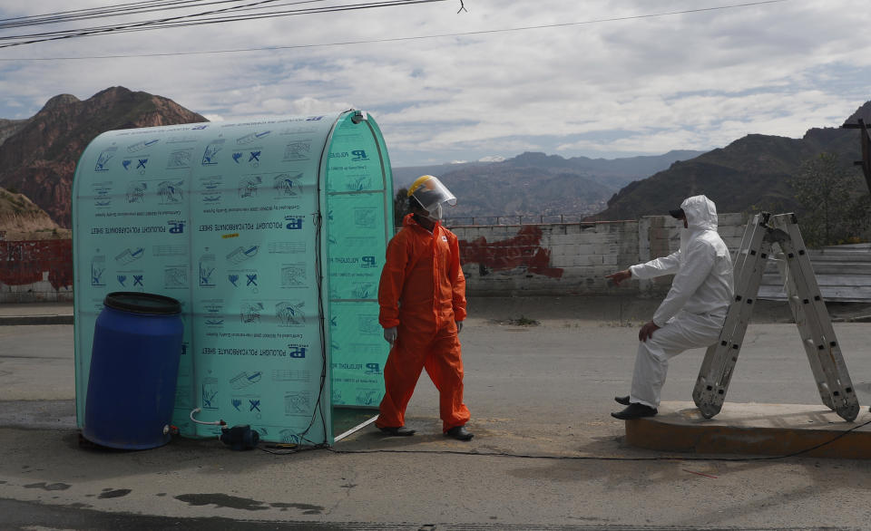 City workers wait for people to walk through a tunnel that sprays disinfectant, in an attempt to contain the spread of the new coronavirus, at the entrance to the community of Mallasa on the outskirts of La Paz, Bolivia, Monday, April 20, 2020. (AP Photo/Juan Karita)