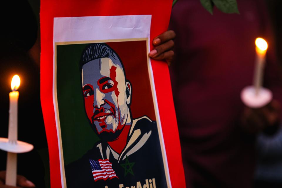 An attendee holds a poster depicting Adil Dghoughi at a vigil in Martindale, Texas on Oct. 24, 2021. Dghoughi was shot and killed in his vehicle by a Martindale, Texas homeowner in early October.