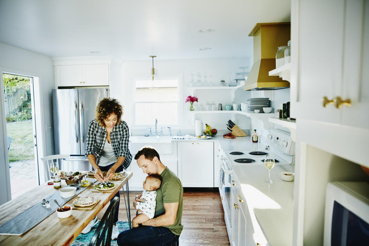 Father holding infant while preparing dinner with wife in kitchen