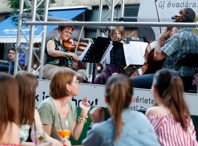 Members of the Budapest Festival Orchestra play music on the back of a truck while driving through the city