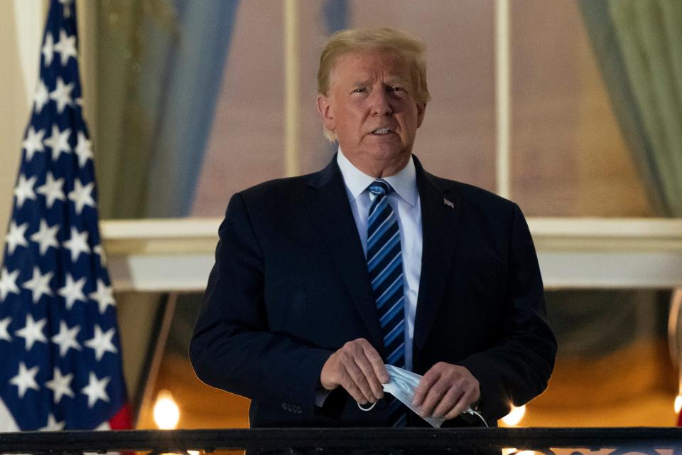 In this Oct. 5 file photo, President Donald Trump removes his mask as he stands on the Blue Room Balcony at the White House.