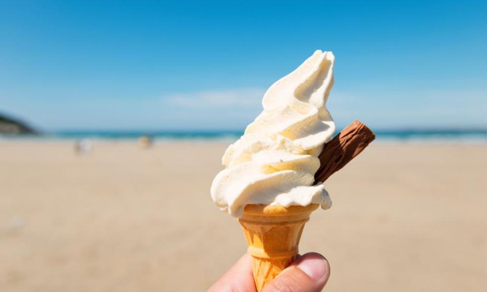 An ice-cream 99 cornet and 'flake' held up against a beach and bright blue sky