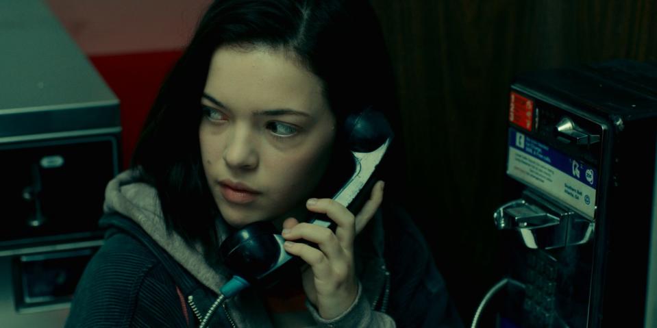 A teenage girl looks over her shoulder while talking on a pay phone.