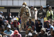 A soldier watches homeless people who were rounded up in downtown Johannesburg Friday, March 27, 2020, after South Africa went into a nationwide lockdown for 21 days in an effort to mitigate the spread to the coronavirus. The new coronavirus causes mild or moderate symptoms for most people, but for some, especially older adults and people with existing health problems, it can cause more severe illness or death. (AP Photo)