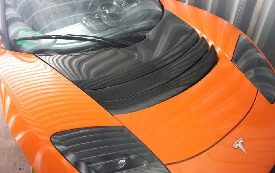 An orange 2010 Tesla Roadster in a shipping container.