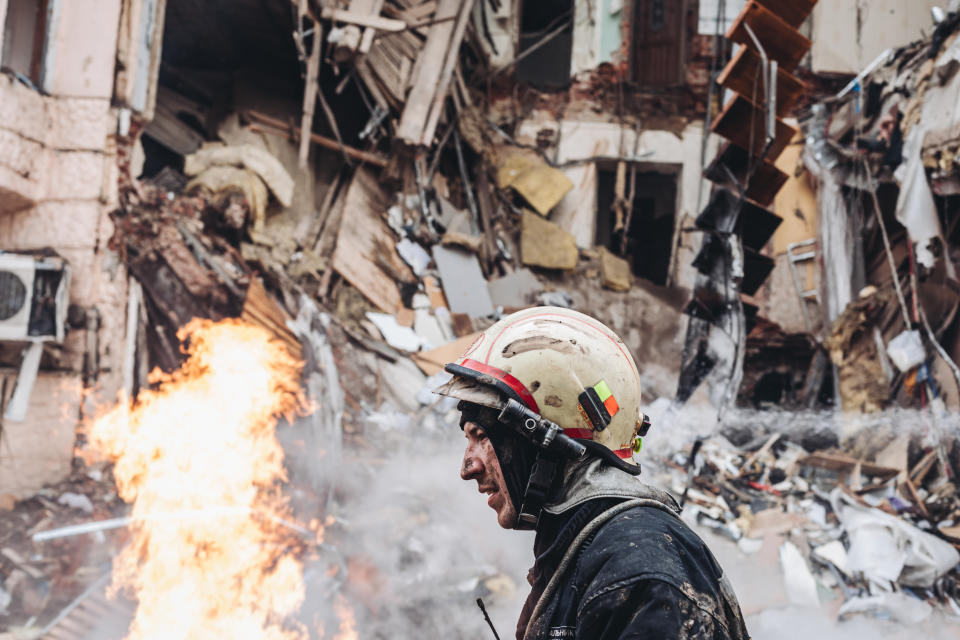 A firefighter passes in front of a building still ablaze after Russian bombing.