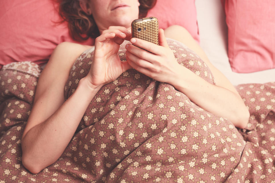 Young woman is lying in bed and sending a text on her phone