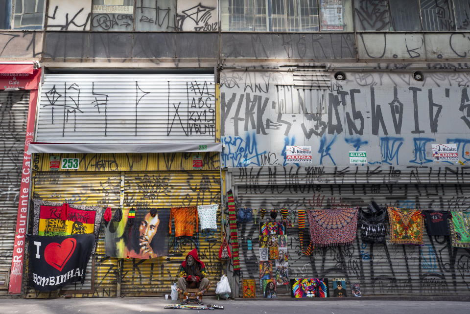 A street vendor sells his merchandise in front of shuttered stores on a sidewalk left empty due to a quarantine imposed by the state government to help contain the spread of the new coronavirus in Sao Paulo, Brazil, Monday, April 27, 2020. (AP Photo/Andre Penner)