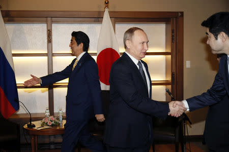 Russian President Vladimir Putin shakes hands with a Japanese official as Japanese Prime Minister Shinzo Abe prepares to greet a delegate during their meeting in Nagato, Japan December 15, 2016. REUTERS/Alexander Zemlianichenko/Pool