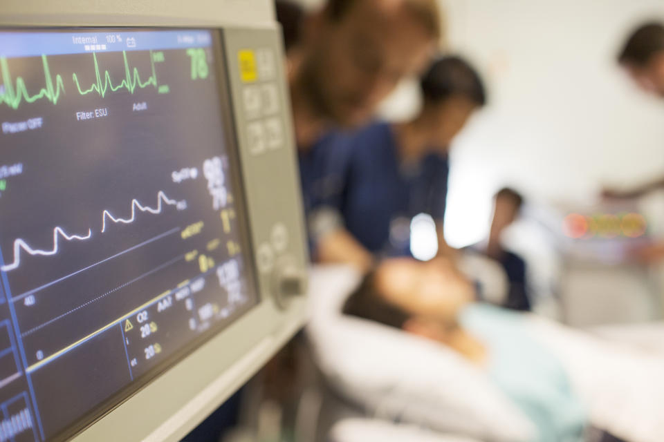 Healthcare professionals attend to a patient in a hospital bed, with medical monitors displaying vital signs in the foreground