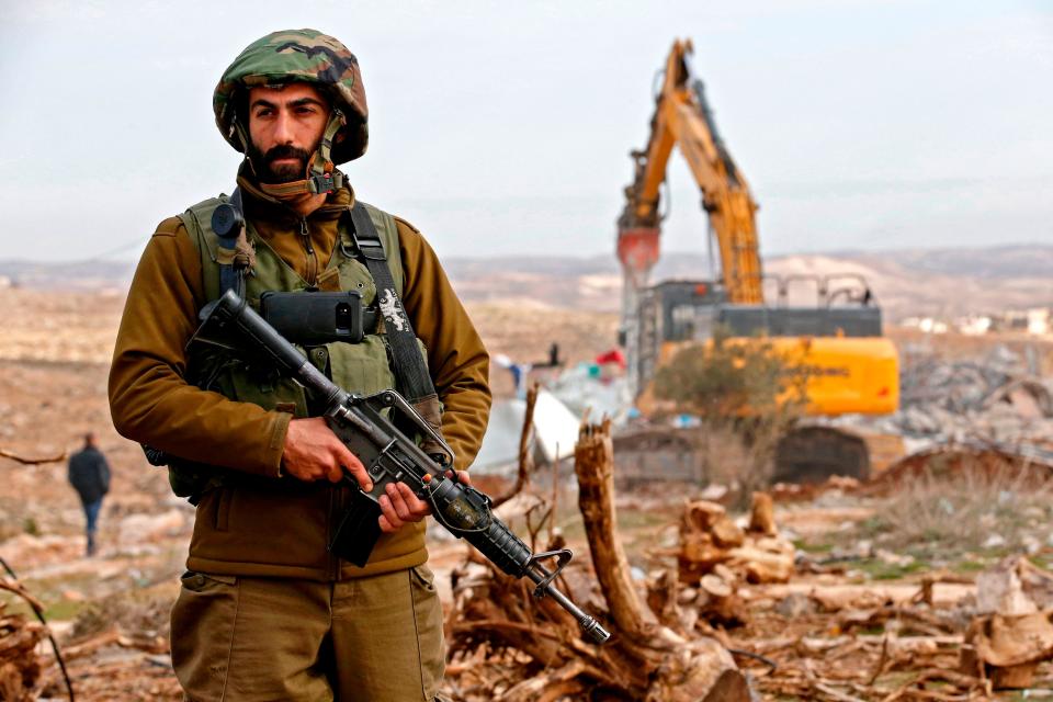 An Israeli soldier stands guard as an excavator demolishes a Palestinian home which Israeli authorities said was build without a permit in the village of Al-Dirat near the West Bank town of Hebron on 16 January, 2020. The Israeli government has approved the construction of hundreds of new homes in West Bank settlements. (AFP via Getty Images)