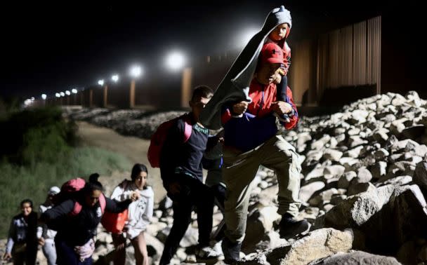 PHOTO: Immigrants seeking asylum in the United States walk along the border fence on their way to be processed by U.S. Border Patrol agents in the early morning hours after crossing into Arizona from Mexico on May 11, 2023 in Yuma, Ariz. (Mario Tama/Getty Images)