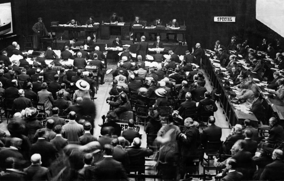 a black and white photo of several people seated in a room listening to testimony from a witness