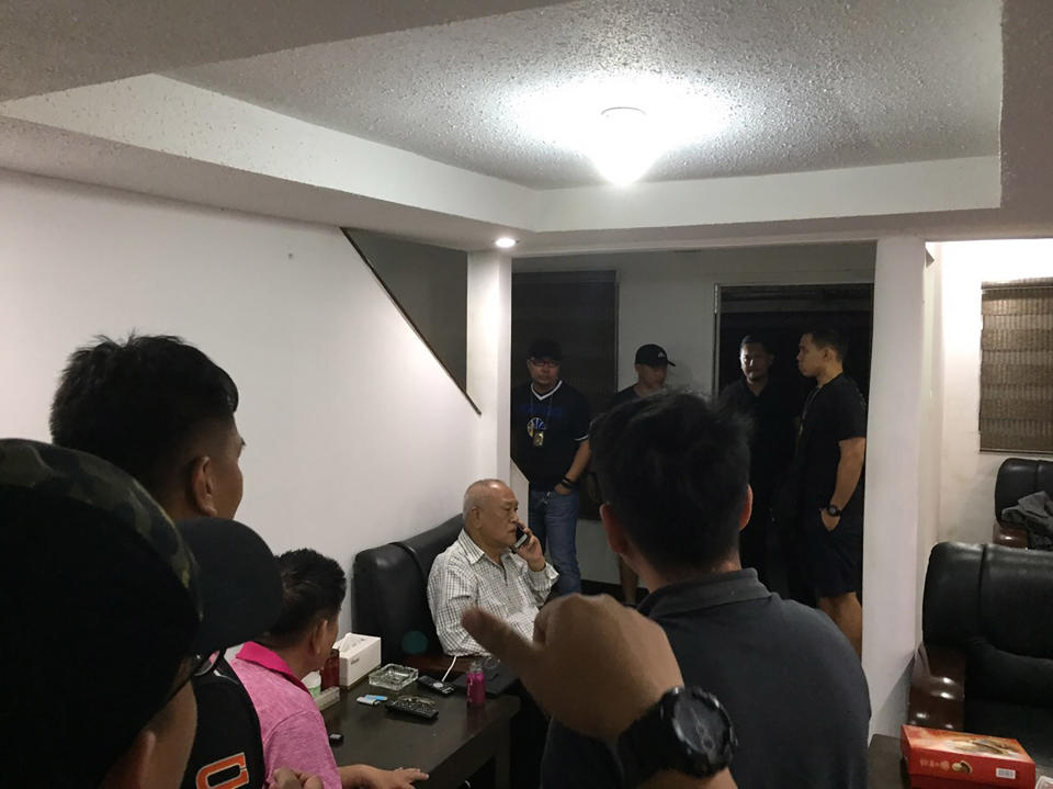 警方與移民局幹員16日在蘇比克灣一座別墅內逮捕吳健保（打電話者）。吳健保見到菲國執法人員，相當錯愕。（中央社/菲國警方提供）