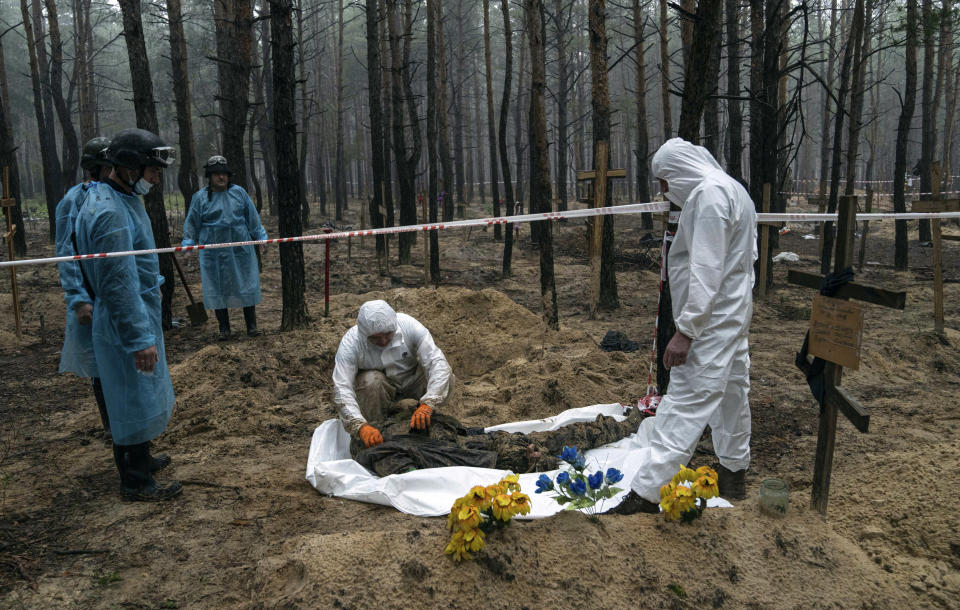 Experts search the body of a Ukrainian soldier during an exhumation in the recently retaken area of Izium, Ukraine, Friday, Sept. 16, 2022. Ukrainian authorities discovered a mass burial site near the recaptured city of Izium that contained hundreds of graves. It was not clear who was buried in many of the plots or how all of them died, though witnesses and a Ukrainian investigator said some were shot and others were killed by artillery fire, mines or airstrikes. (AP Photo/Evgeniy Maloletka)