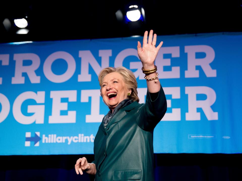 Hillary Clinton waves at a campaign event in Washington, DC. A banner in the background says "Stronger Together."