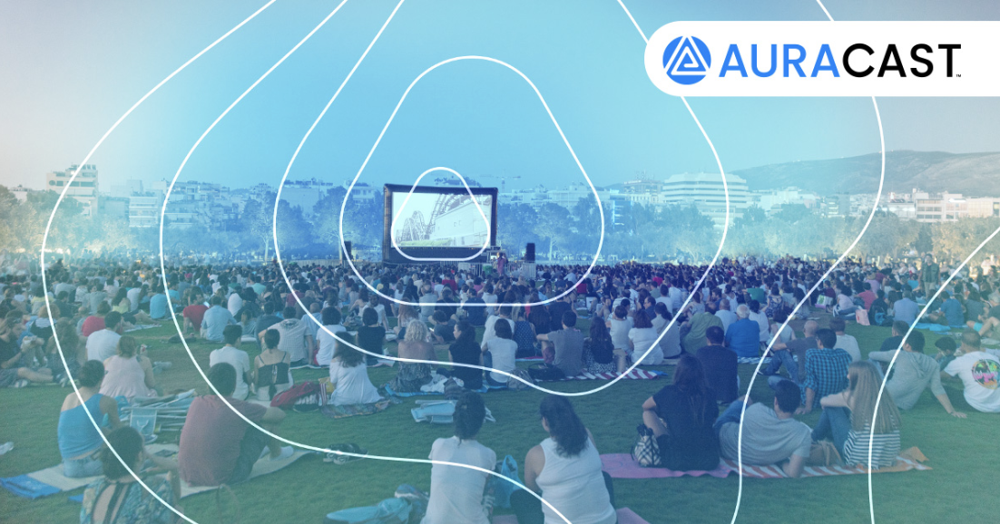  Bluetooth Auracast being used at a music festival, on a big screen with people watching and listening 
