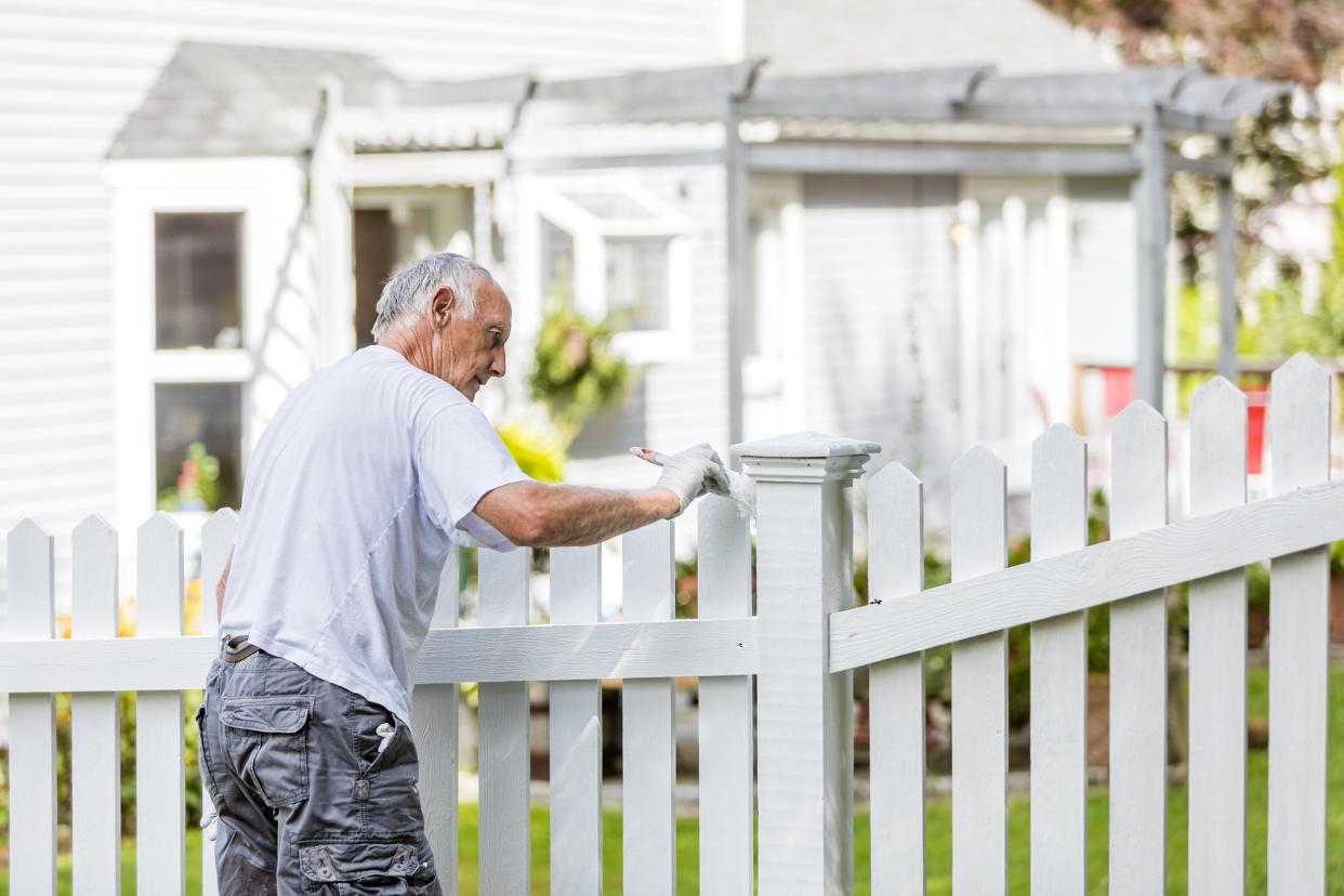 senior man painting a white picket fence