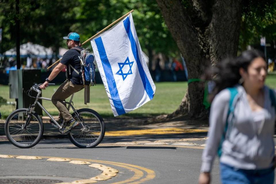 A cyclist carries an Israel flag as he rides near a pro-Palestinian encampment on the UC Davis quad on Monday.