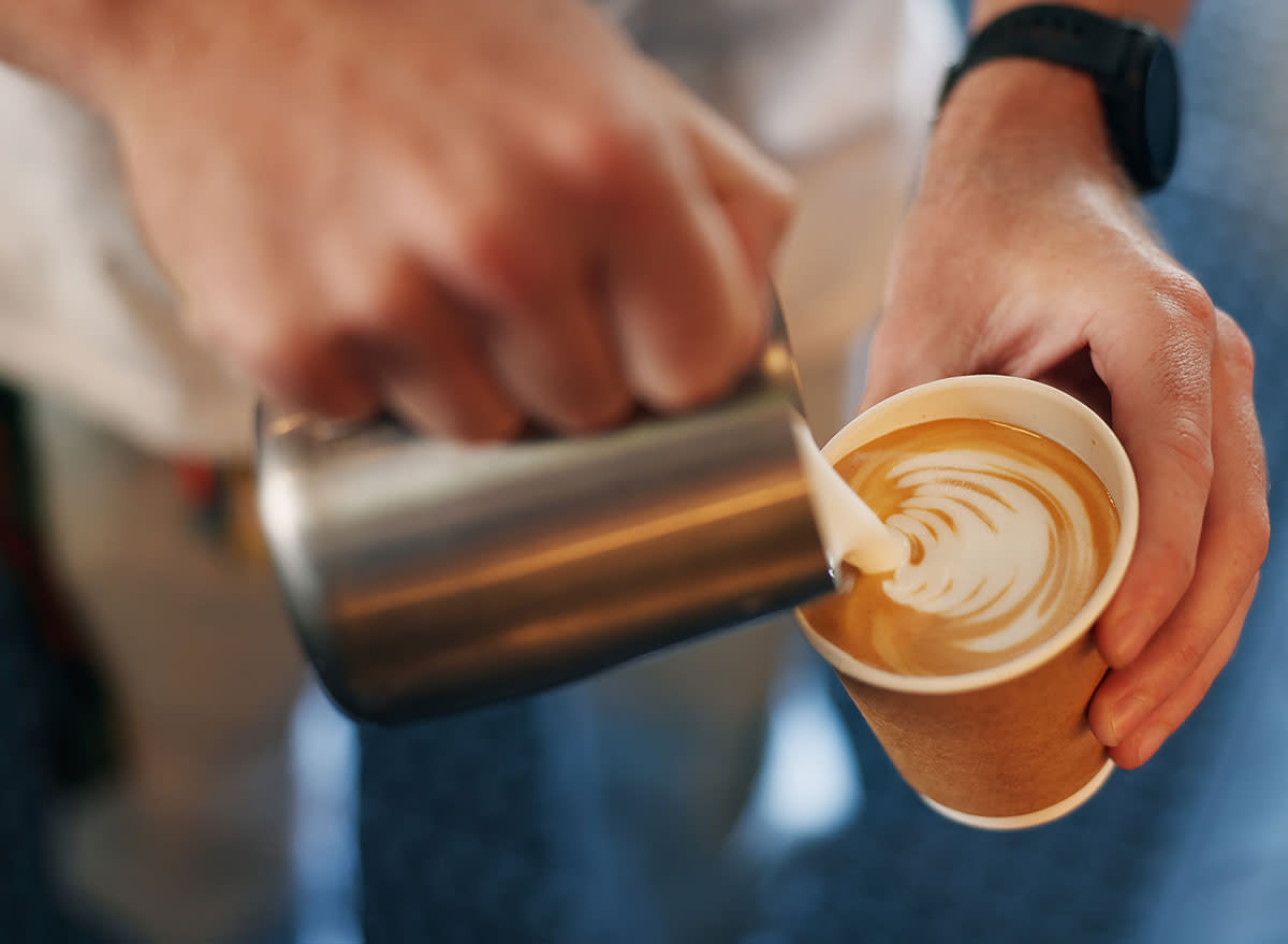 A closeup of a coffee shop barista pouring an artfully foamy latte for take away.