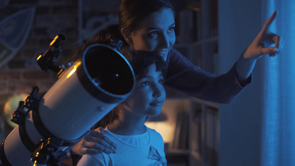 Cute sisters watching the stars together at home using a telescope, family and leisure concept