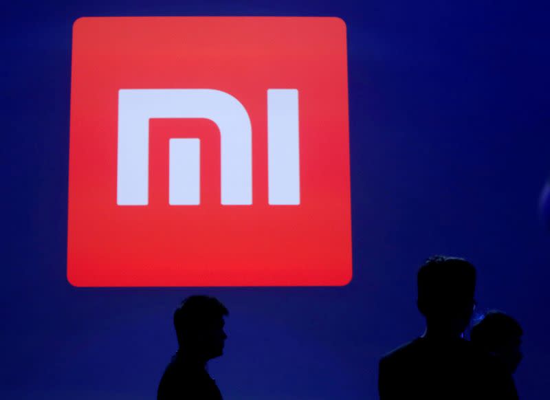 FILE PHOTO: Attendants are silhouetted in front of Xiaomi's logo in Beijing