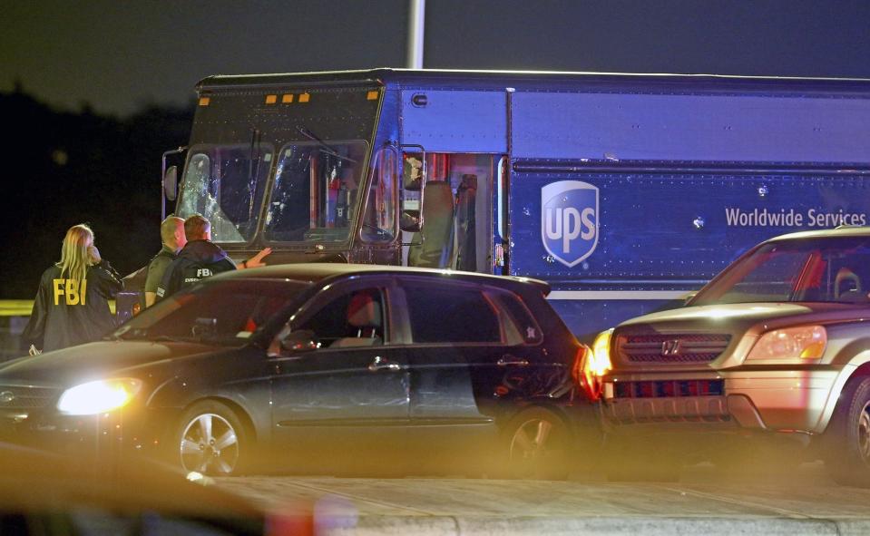 Law enforcement stand near a vehicle that appears to be part of the crime scene where four people were killed, Thursday, Dec. 5, 2019 in Miramar, Fla. The FBI says four people, including a UPS driver, were killed after robbers stole the driver's truck and led police on a chase that ended in gunfire at a busy Florida intersection during rush hour. (Charles Trainor Jr./Miami Herald via AP)