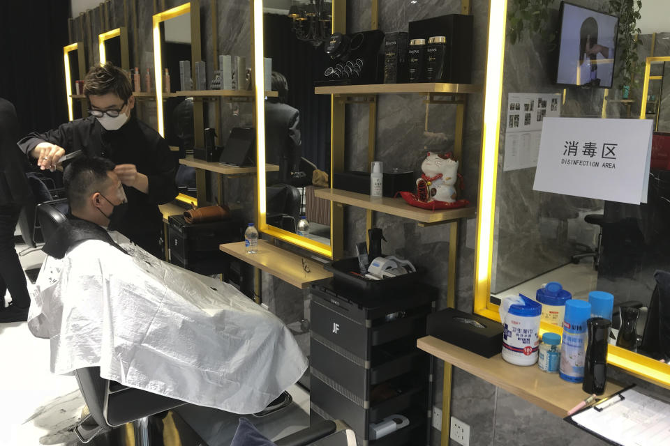 A barber wearing a protective face mask cuts a clients hair near a disinfection notice at a hair salon in Beijing, Monday, Feb. 24, 2020. Monday is the second day of the second month of the Chinese lunar calendar, traditionally an auspicious time when people rush into barbershops to get new haircuts. Getting a fresh look on the day is thought to bring good luck for the year ahead, but getting a haircut has become a challenge in China now that most barbershops are temporarily shut to avoid public gatherings amid the virus outbreak. (AP Photo/Olivia Zhang)