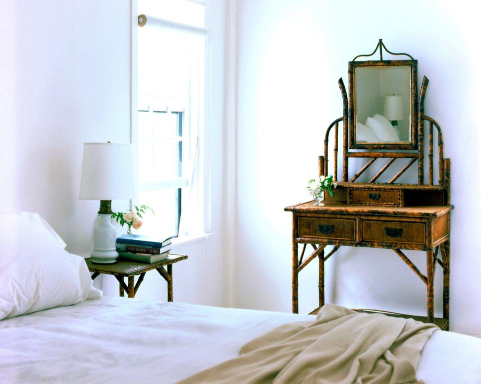 A neutral colored bedroom with a wooden vanity opposite the window