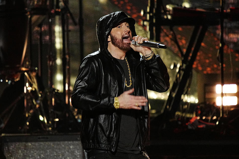 Eminem performing on stage, wearing a black hoodie and gold chains