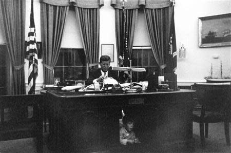 Former United States President John F. Kennedy sits as his desk in the Oval Office while his son, John F. Kennedy Jr., looks out from underneath, at the White House in Washington in this handout image taken on October 17, 1963. REUTERS/Cecil Stoughton/The White House/John F. Kennedy Presidential Library