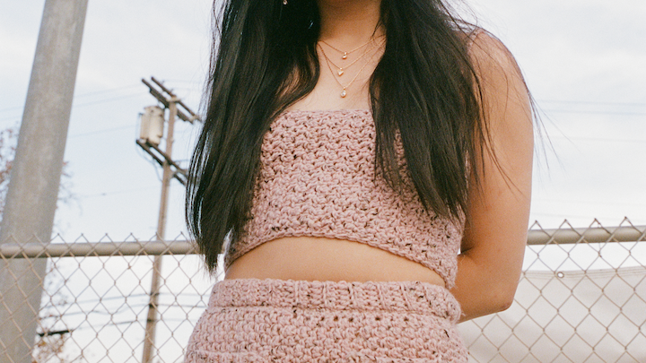 jess hong posing in a crochet pink top and skirt