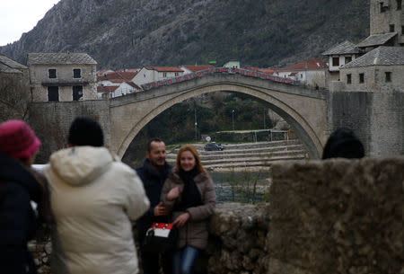 People taking pictures in front of Old Bridge where a poster reads: "The old bridge surfaced for the ones who love it" are seen during a television broadcast of the appeal trial in the Hague, Netherlands, for six Bosnian Croat senior wartime officials accused of war crimes against Muslims in Bosnia's 1992-1995 war, in Mostar, Bosnia and Herzegovina November 29, 2017. REUTERS/Dado Ruvic
