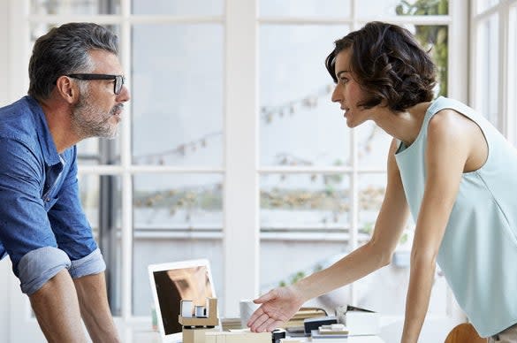 a man and woman leaning over a desk and have a conversation