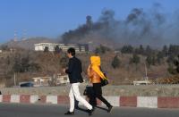 <p>Afghans walk near the Intercontinental Hotel as smoke billows during a fight between gunmen and Afghan security forces in Kabul on January 21, 2018. (Photo: Wakil Kohsar/AFP/Getty Images) </p>