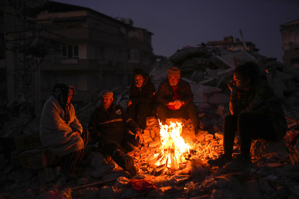 A family keeps warm by a fire as they follow a rescue team searching for relatives in earthquake-destroyed buildings in Antakya, southern Turkey, Wednesday, Feb. 15, 2023. (AP Photo/Francisco Seco)