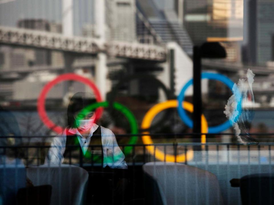 A hotel waitress wearing a face mask amid the coronavirus outbreak as the Olympic rings reflect off a window: AP