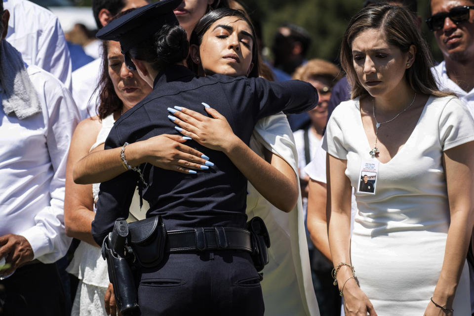 A Los Angeles Police Department officer hugs Anahi Diaz, center, after placing a flower on her brother Officer Juan Jose Diaz's coffin during the funeral at Forest Lawn Hollywood Hills cemetery, Monday, Aug. 12, 2019, in Los Angeles. Diaz was killed while off duty in Lincoln Heights after visiting a taco stand. (Sarah Reingewirtz/The Orange County Register via AP)