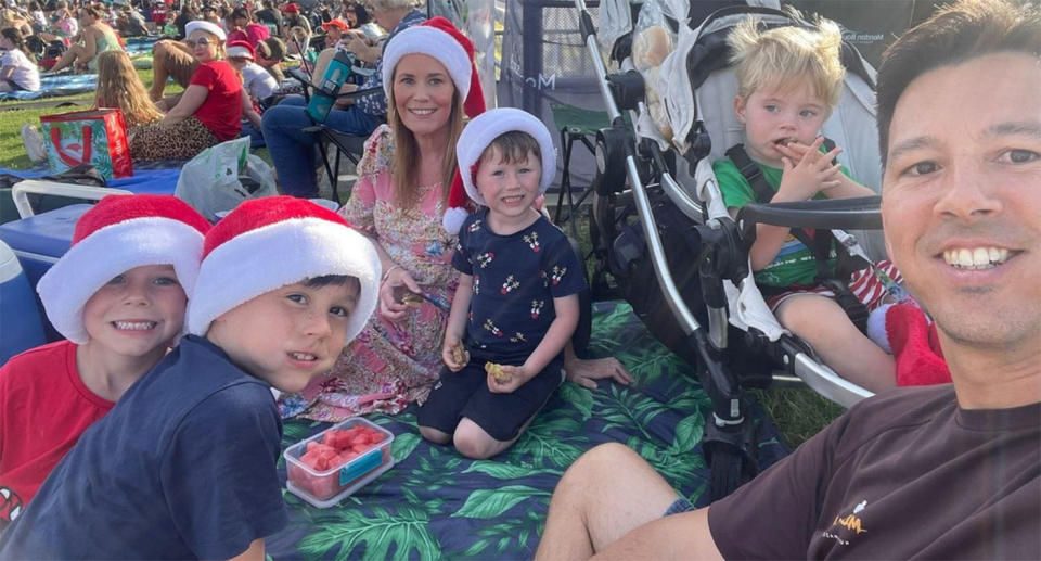 The Thompson family wears Christmas hats as they sit on a rug at Carols by Candlelight