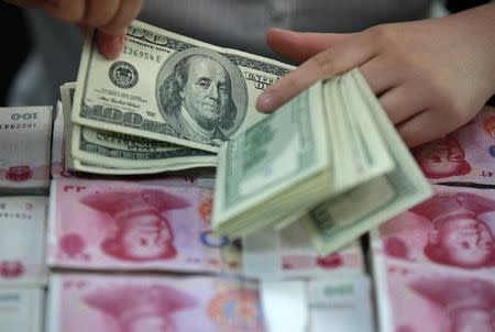 A bank clerk counts U.S. dollar banknotes on bundles of 100 Chinese yuan banknotes at a branch of a bank in Huaibei, Anhui province April 26, 2012. REUTERS/Stringer