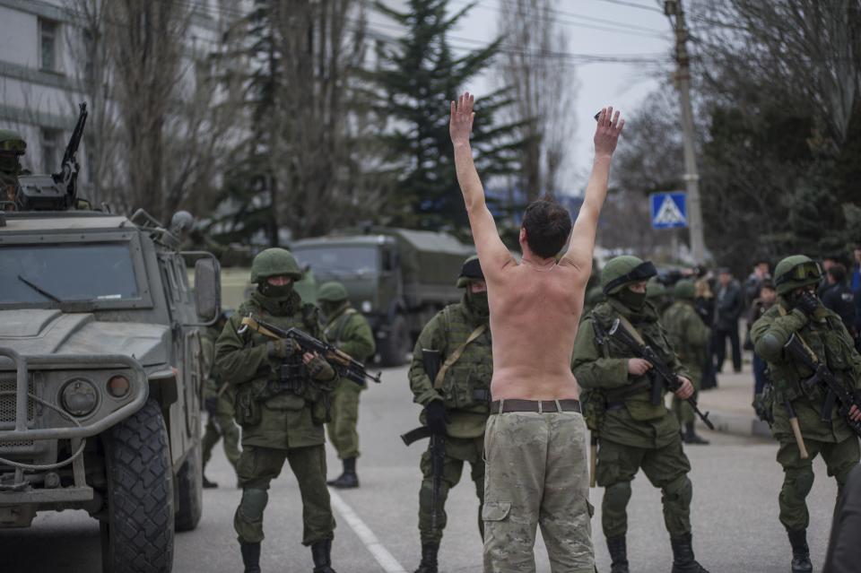 FILE - In this Saturday, March 1, 2014 file photo, a Ukrainian man stands in protest in front of gunmen in unmarked uniforms as they stand guard in balaklava, on the outskirts of Sevastopol, Crimea. The European Court of Human Rights decided Thursday Jan. 14, 2021, to start considering Ukraine's complaint against alleged human rights violations in the Russia-annexed Crimea. (AP Photo/Andrew Lubimov, File)