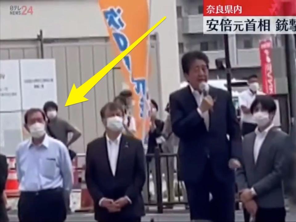 Still from TV footage showing Shinzo Abe assassination suspect standing behind Abe moments before the shooting