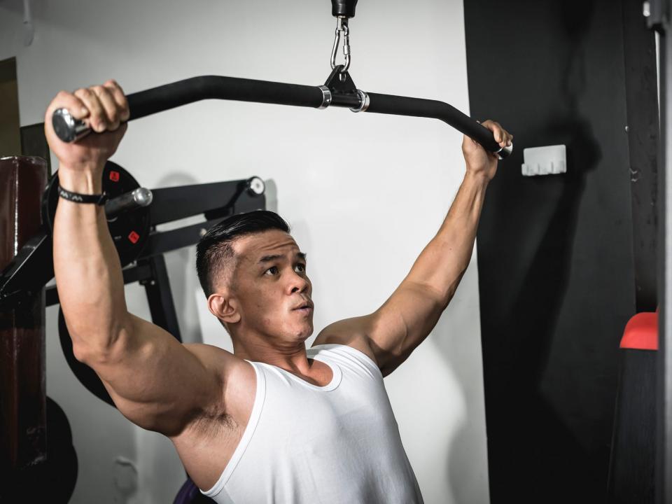 a man in a tank top performing a lat pulldown exercise at the gym with an exercise machine