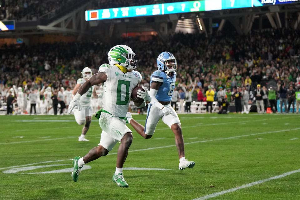 Oregon Duck running back Bucky Irving (0), center, is pursued by North Carolina Tar Heels defensive back Lejond Cavazos (6) on a 66-yard touchdown run in the first half of the 2022 Holiday Bowl at Petco Park.