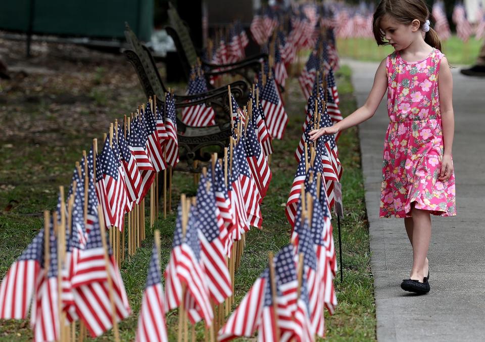 Jane Fitzgerald touches the tops of the flags as she walks along the sidewalk in the garden of the National Museum of the Mighty 8th Air Force on Friday, May 26, 2023. Each one of the 26,000 flags honors an airman lost during WWII.