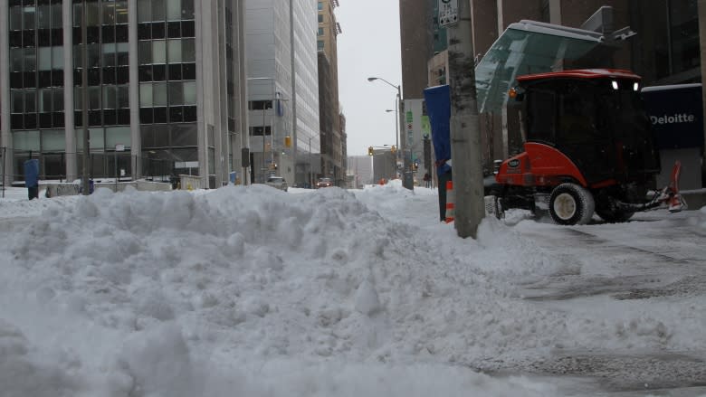 A Bobcat snow plow clears the sidewalk along Queen Street in front of the World Exchange Plaza in Ottawa as snow piles up in one of the street's lanes.