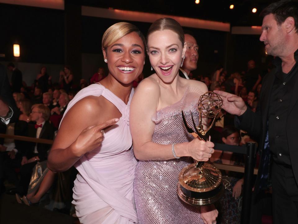 ariana debose, smiling, points at amanda seyfriend, who is grinning widely and holding an emmy award