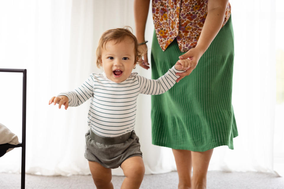 Toddler taking steps holding an adult's hand, expressing joy and achievement