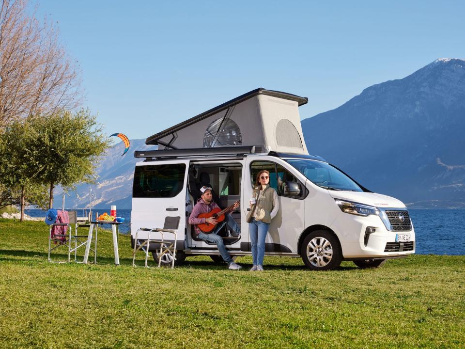 The Nissan Seaside by Dethleff camper van parked as two people hang out around the van. The roof is popped.